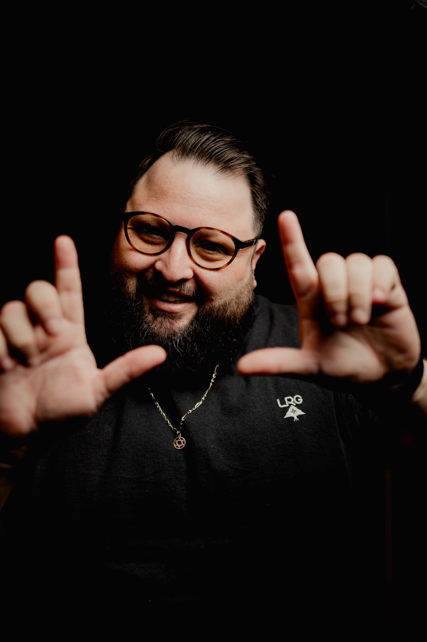 Júnior Ribeiro sorrindo e fazendo um enquadramento com as mãos